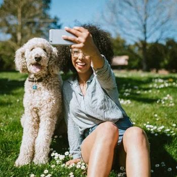 a woman sitting in the grass with her dog taking a picture with her cell phone  at Pinnacle Apartments, Florida