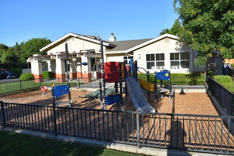 A playground with a slide and a house in the background.