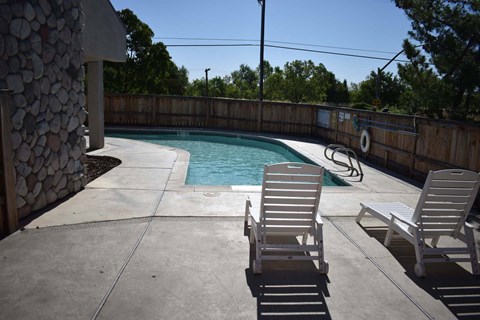 A pool with two chairs and a stone wall.