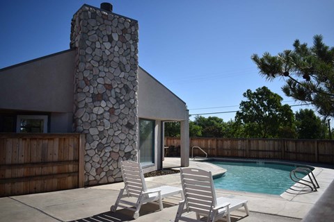 Two chairs are placed on a patio in front of a stone pillar and a pool.