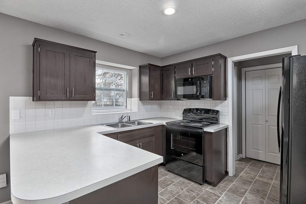 A kitchen with a white counter top and dark brown cabinets.