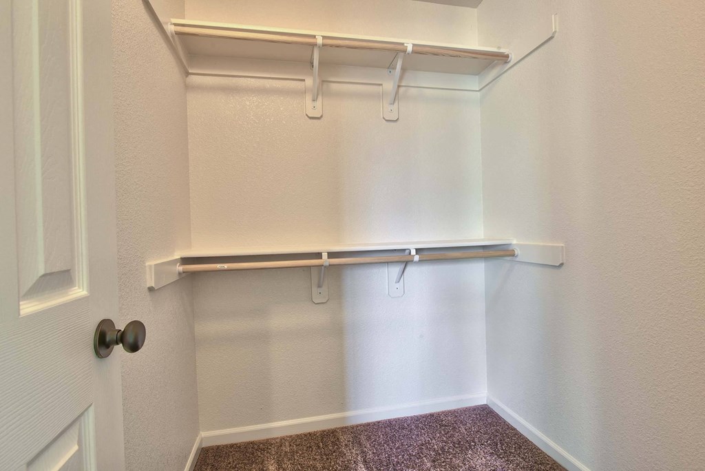 a walk in closet with a hanging rail and white walls