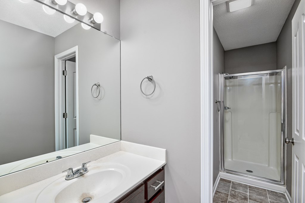 A bathroom with a sink, mirror, and shower.
