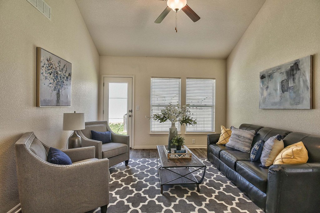 A living room with a black couch, a grey armchair, a coffee table, and a ceiling fan.