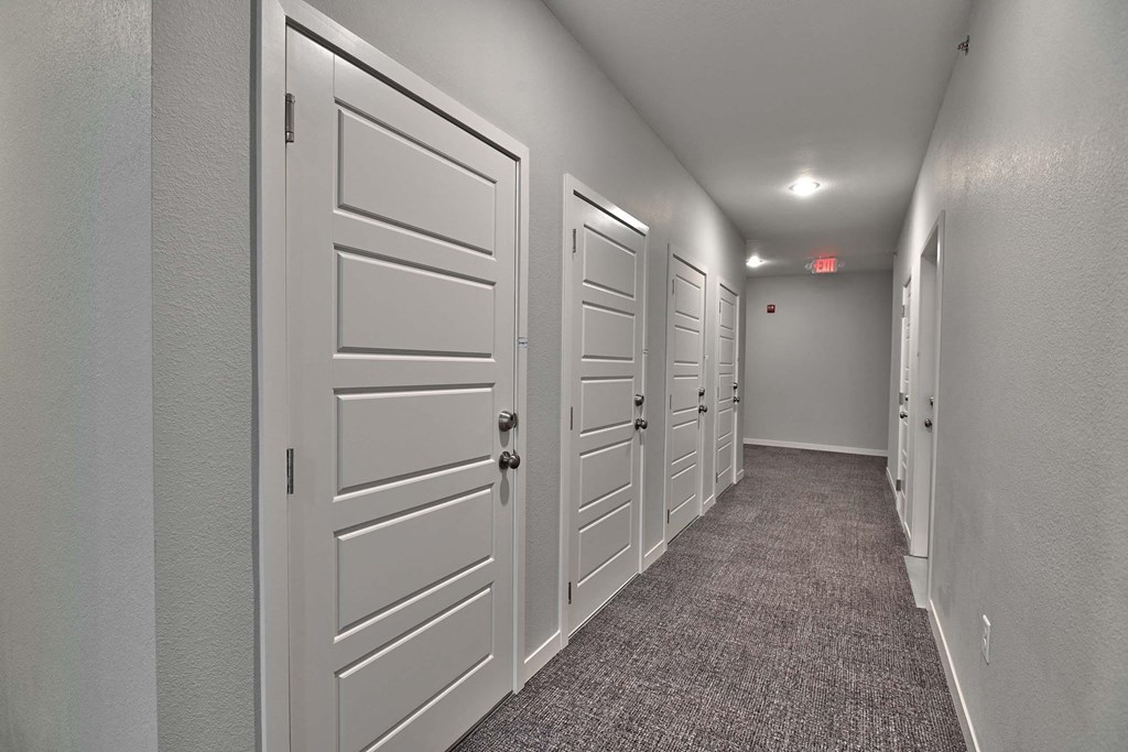 a long hallway with white doors and carpeted floors