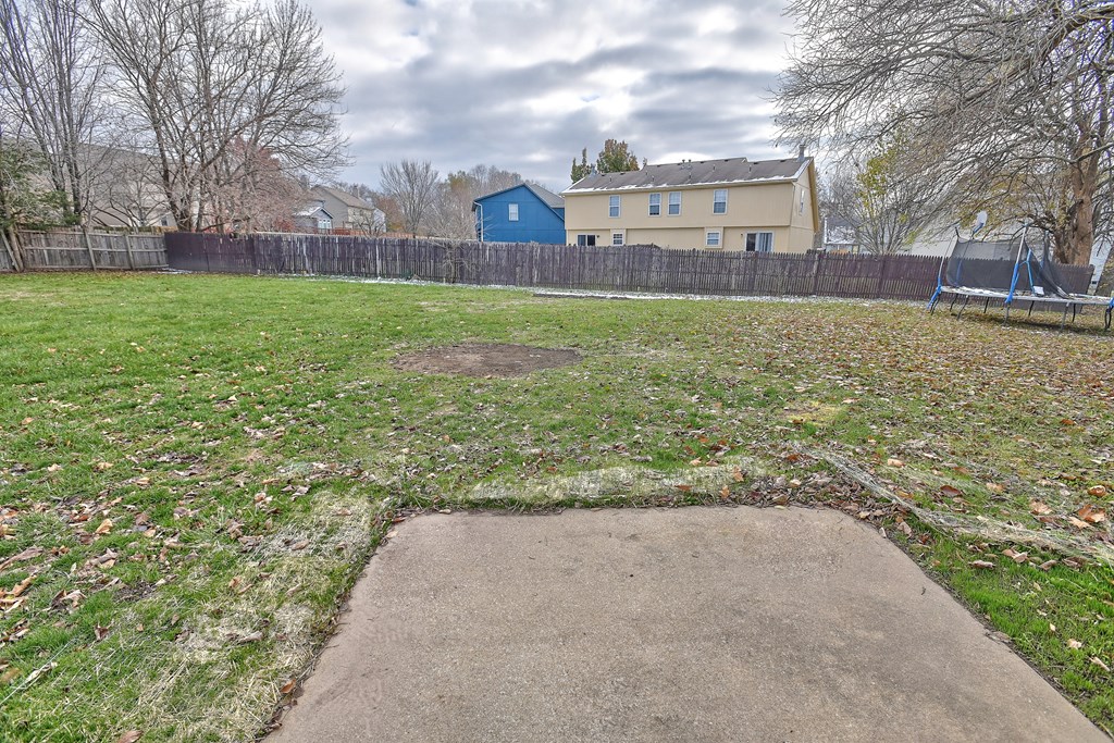 A backyard with a concrete slab in the middle and a fence surrounding it.