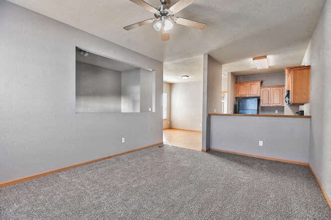 an empty living room with a ceiling fan and a kitchen