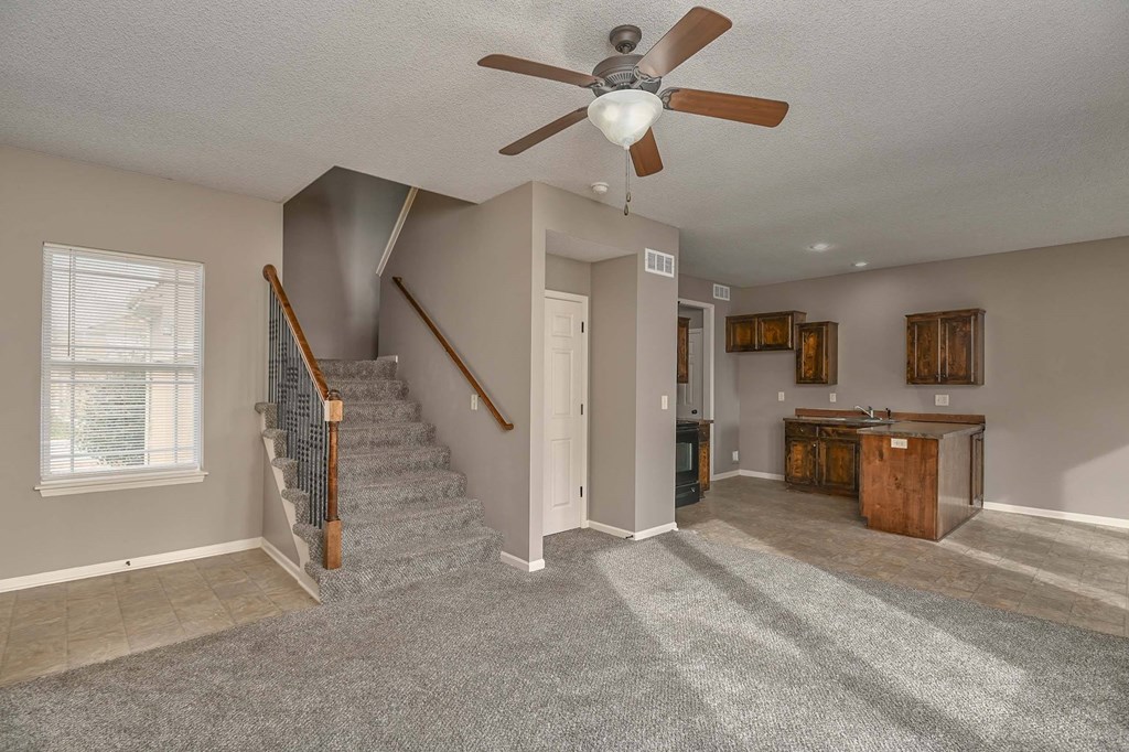 an empty living room with a ceiling fan and stairs