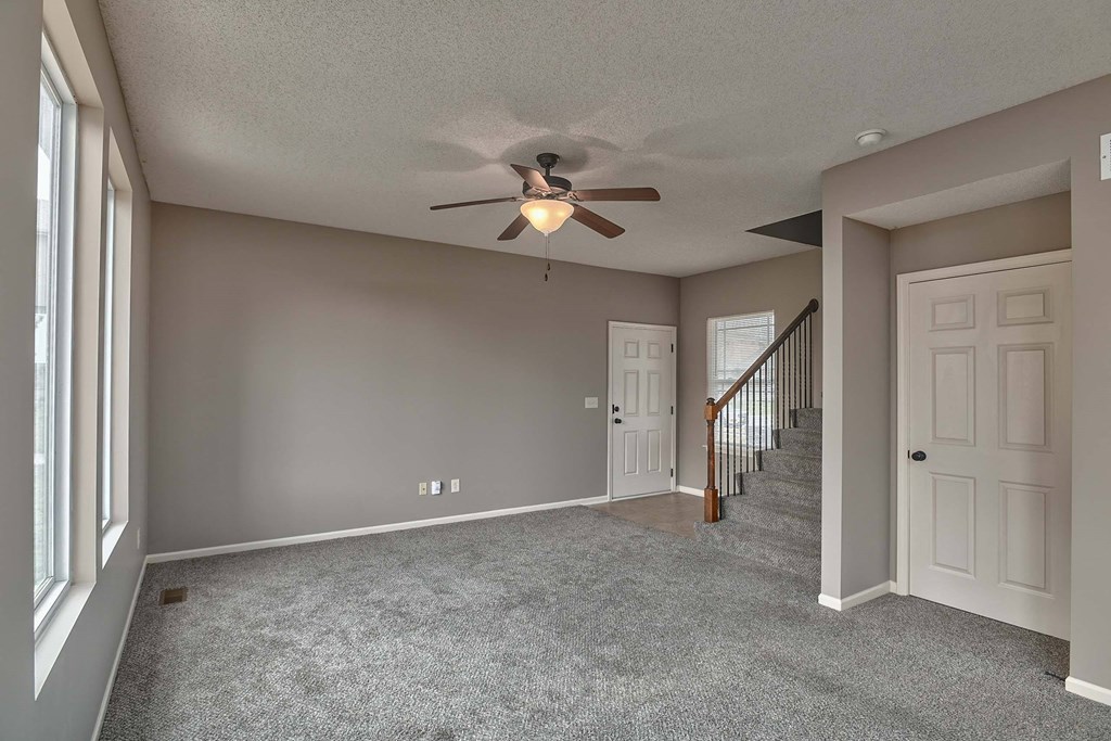 an empty living room with a ceiling fan and a staircase