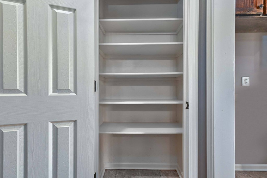 a walk in closet with white shelves and a door