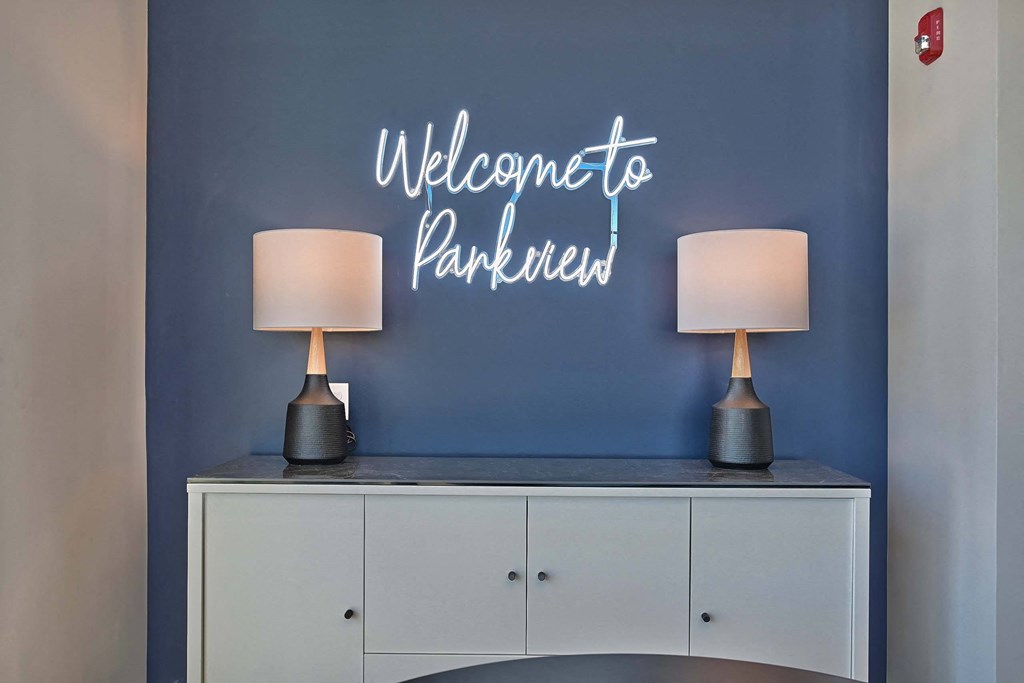 a blue wall with a welcome paralleled neon sign above a white cabinet with lamps