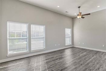 an empty living room with a ceiling fan and three windows