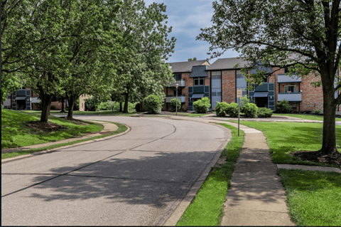A curved road with a sidewalk and trees in front of apartment buildings.