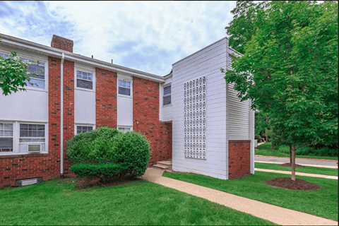 A white building with a brick wall and a green bush in front.