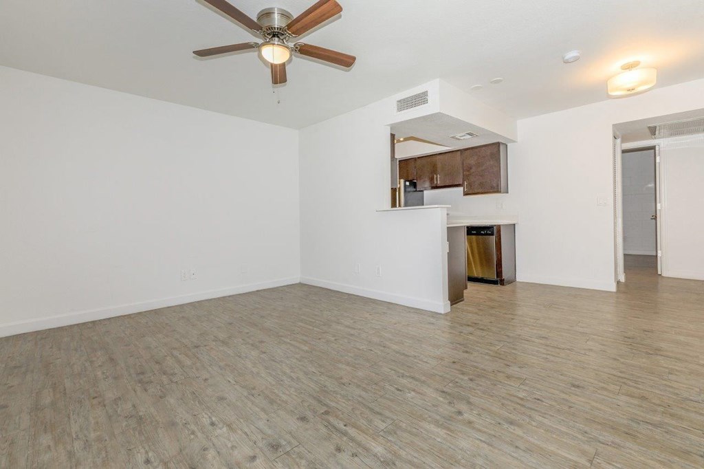 A room with a ceiling fan and a kitchenette in the background.