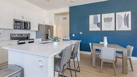 A kitchen with a white island and grey chairs.