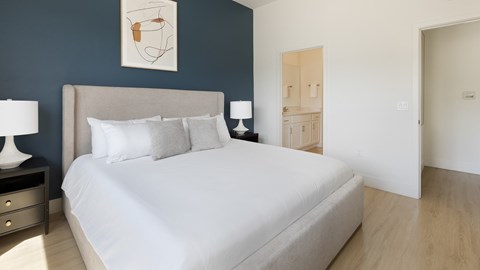 A bed with a white sheet and two pillows sits in a room with a wooden floor.