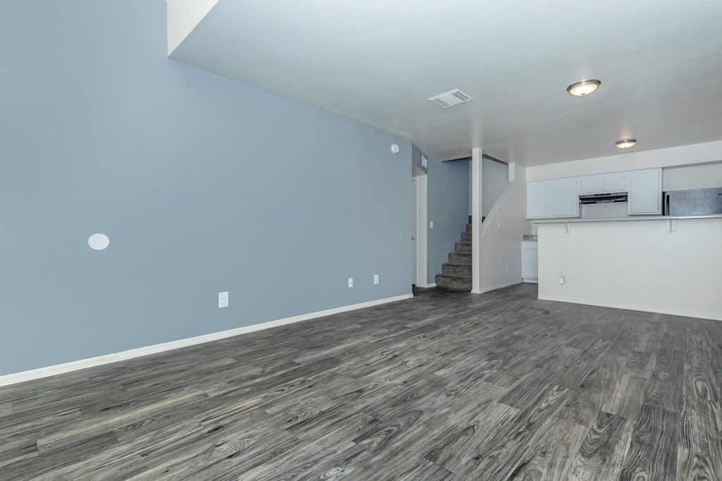 A room with wooden flooring and a staircase in the background.