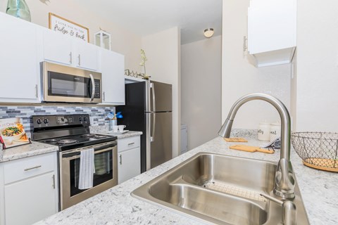 A kitchen with a stainless steel sink and white cabinets.