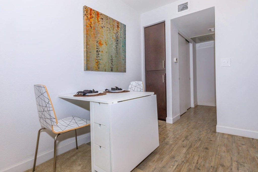 A room with a white desk and a chair with a white and orange patterned seat.