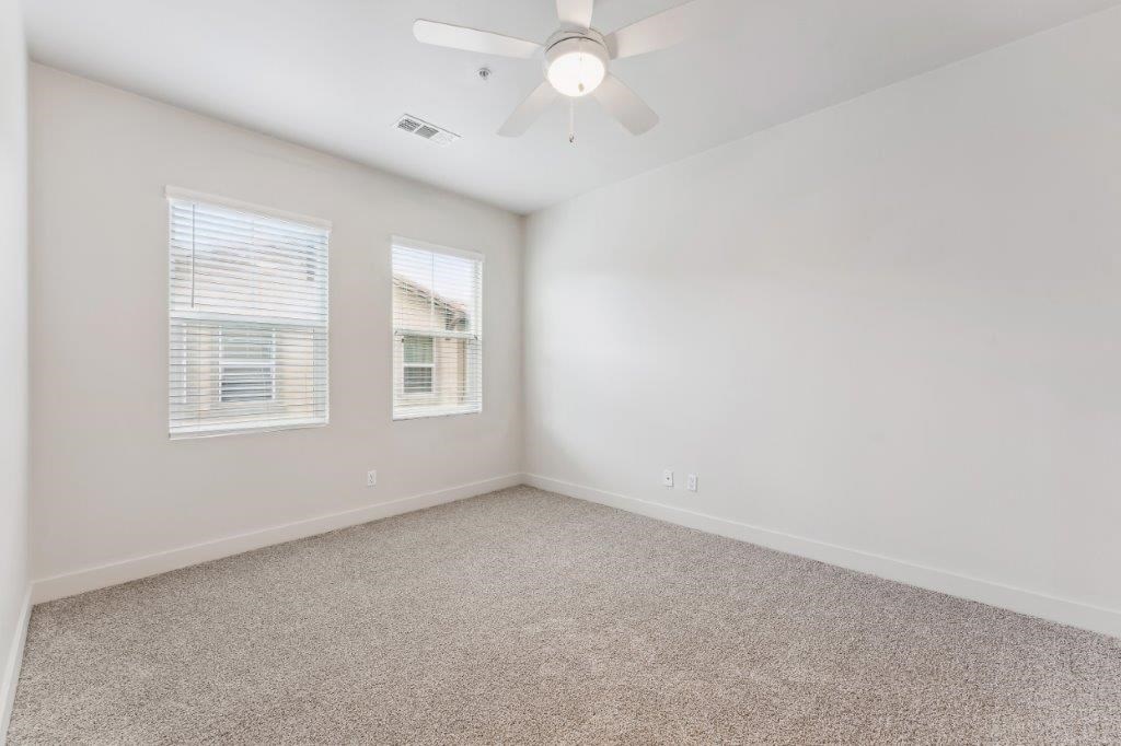 an empty living room with a ceiling fan and two windows