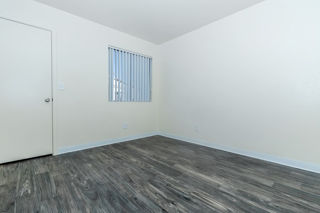 A room with a wooden floor and a window with blinds.