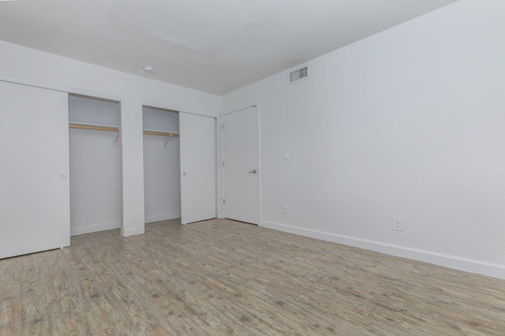A room with white walls and wood flooring with a door and a window.