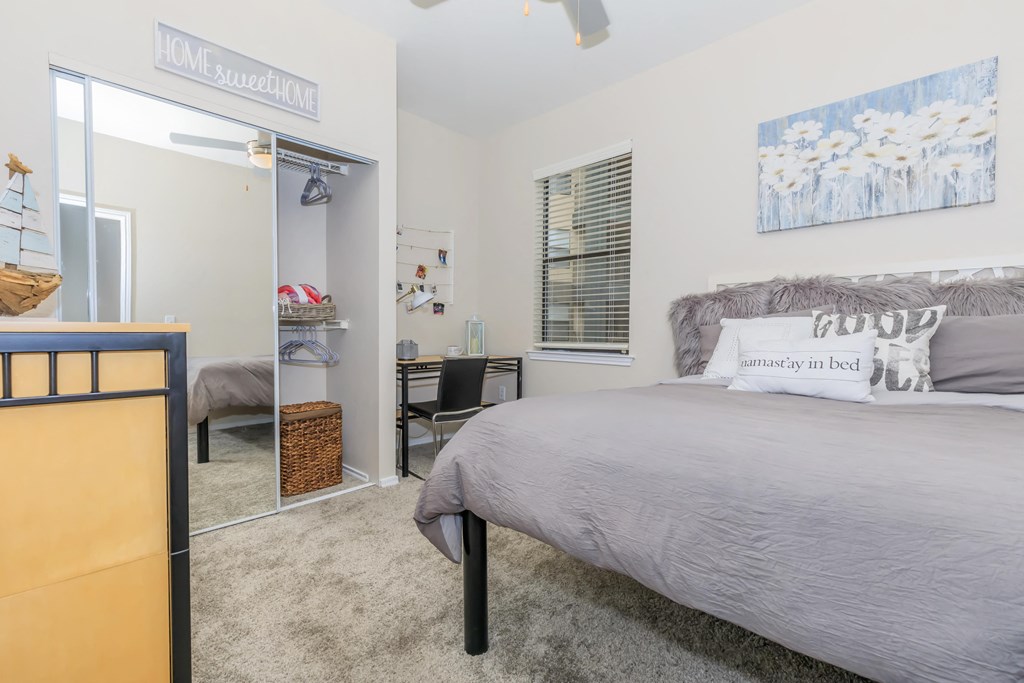 A bedroom with a bed, desk, and a mirrored closet.