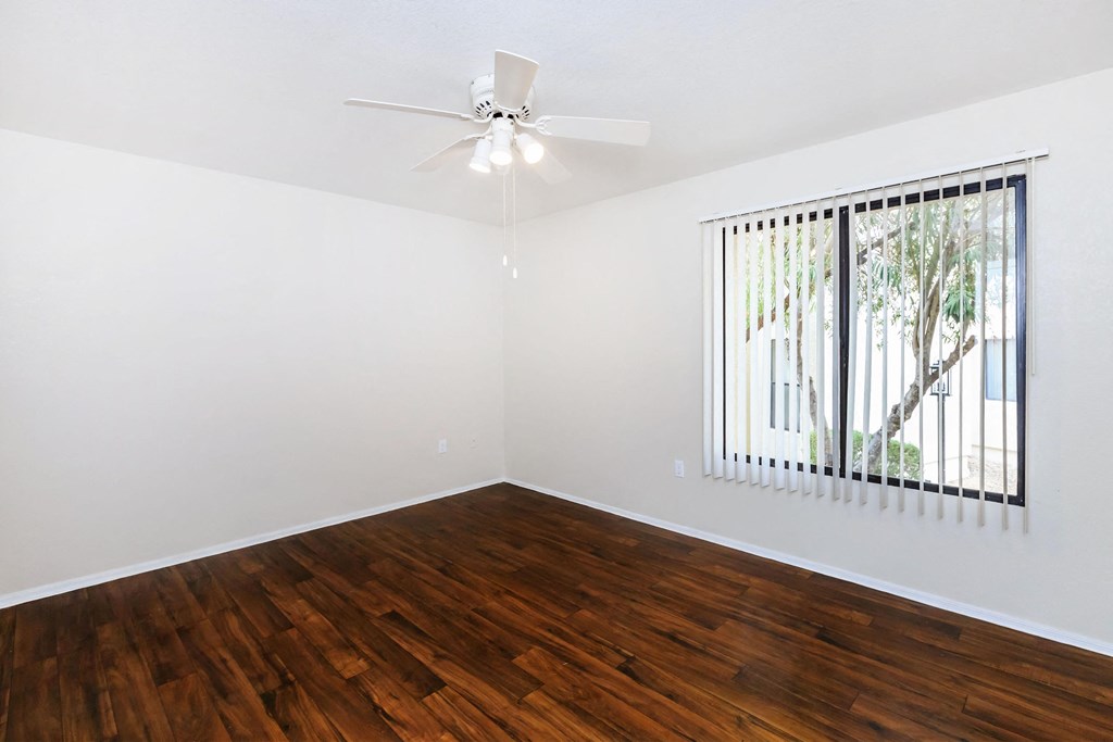 A room with a ceiling fan and a window with a view of a tree.
