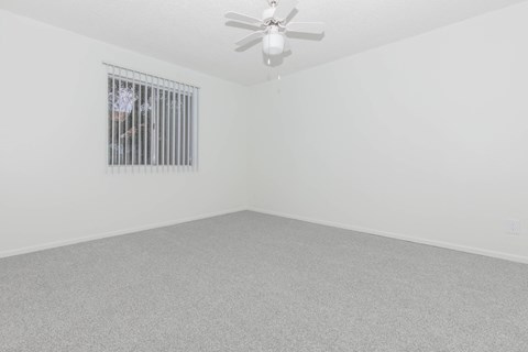 A room with a ceiling fan and a window with bars.
