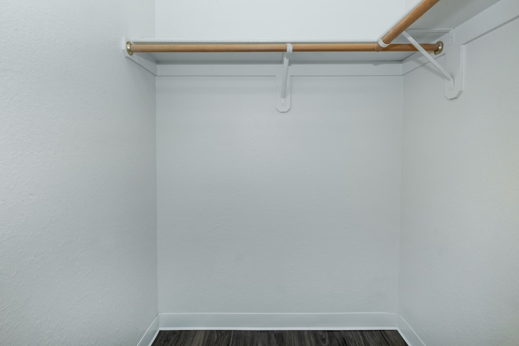A white wall with a shelf and a wooden floor.