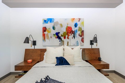 A bedroom with a large painting on the wall and a bed with white bedding.
