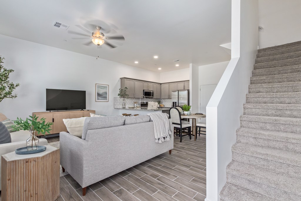 A living room with a grey couch, a television, a plant, and a staircase.