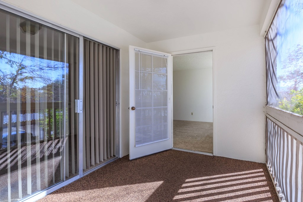A room with a carpet floor, a white door, and a balcony with a railing.