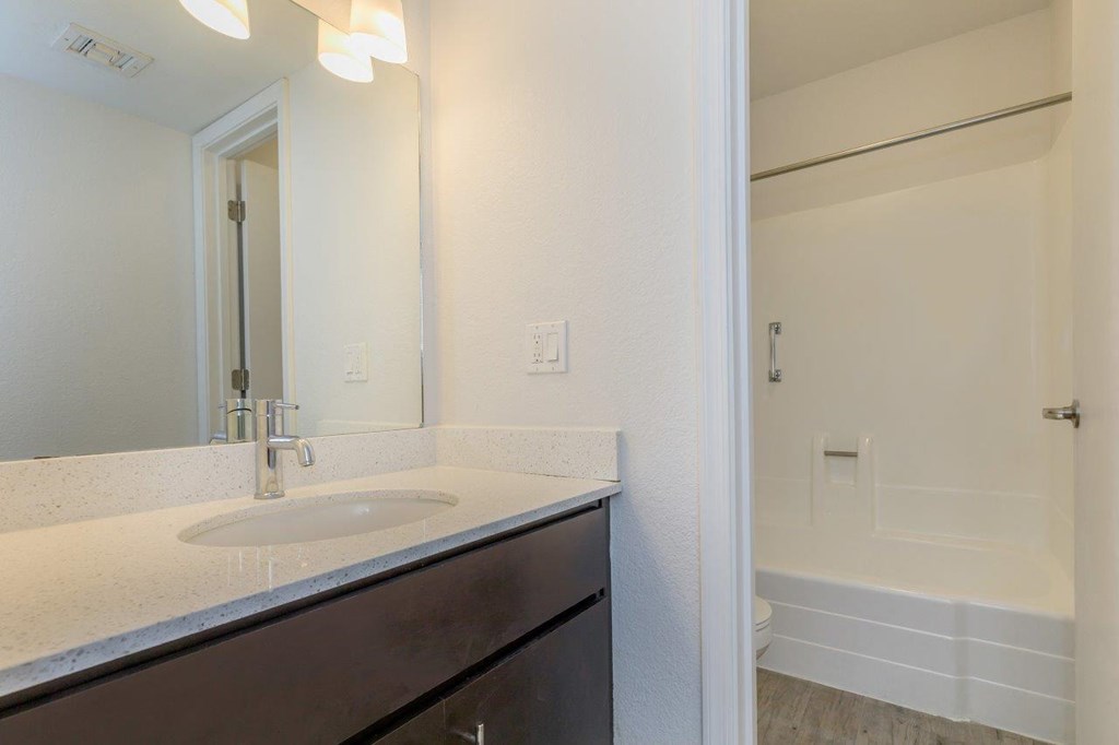 A bathroom with a sink, mirror, and bathtub.