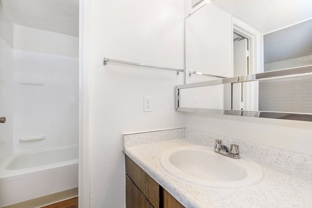 A white bathroom with a sink, mirror, and bathtub.