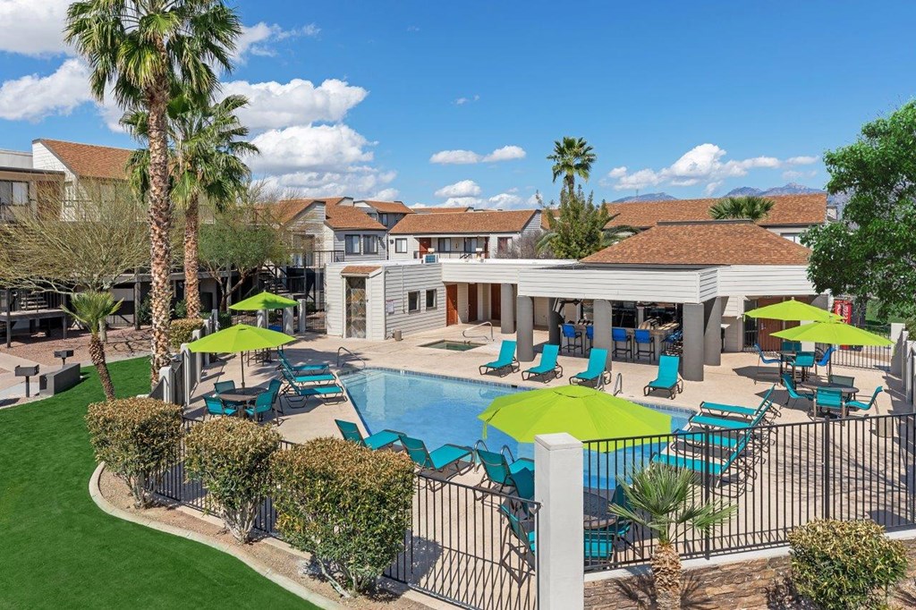 A pool area with a green umbrella and blue chairs.