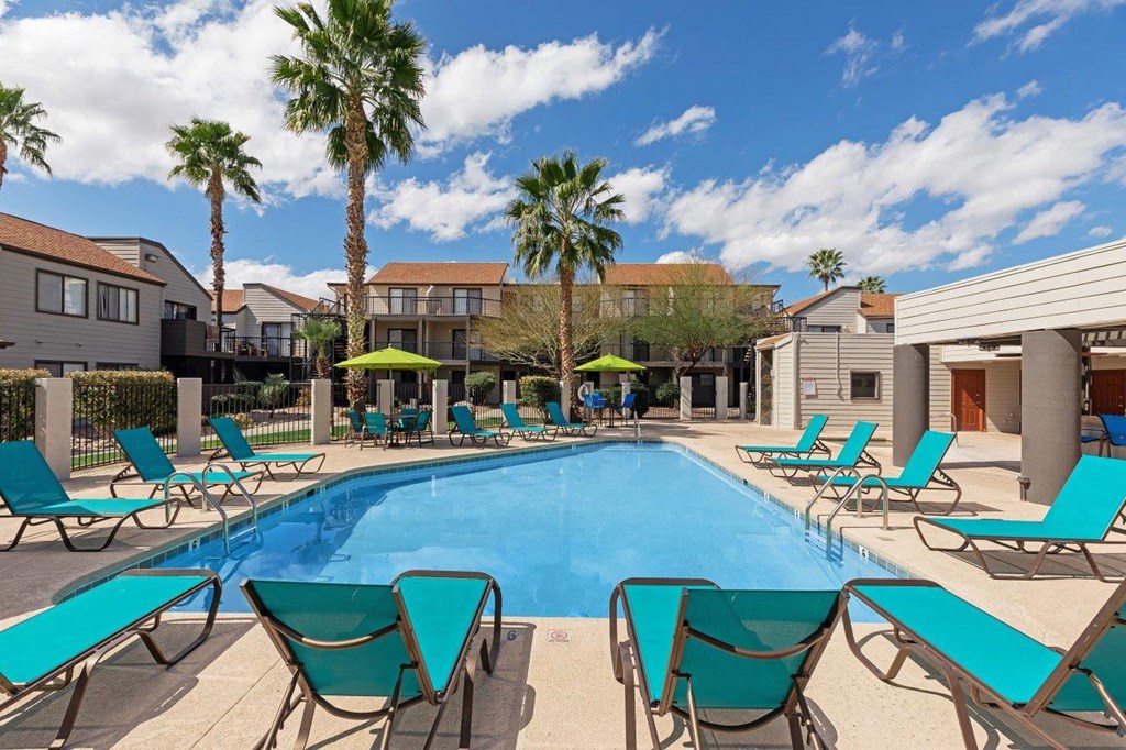 A pool surrounded by lounge chairs and palm trees.