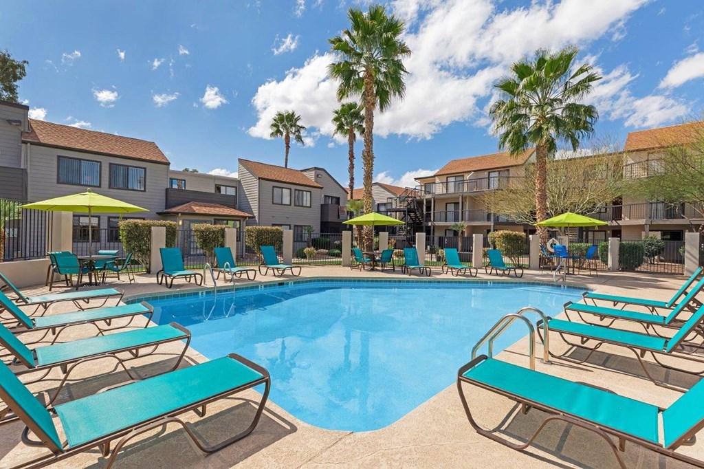 A pool surrounded by sun loungers and palm trees.