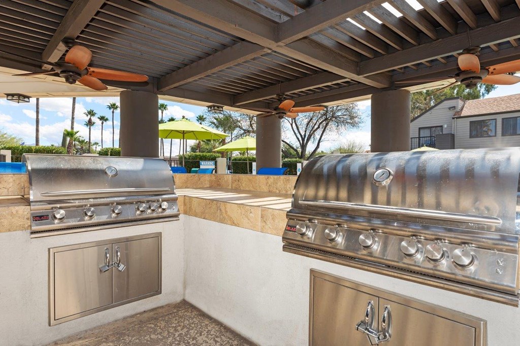 A stainless steel grill is on a patio with a ceiling fan.