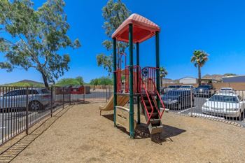 A playground with a red and green structure and a slide.