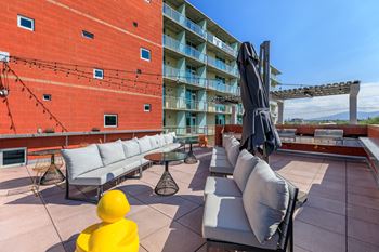A yellow figure stands on a patio with a red building in the background.