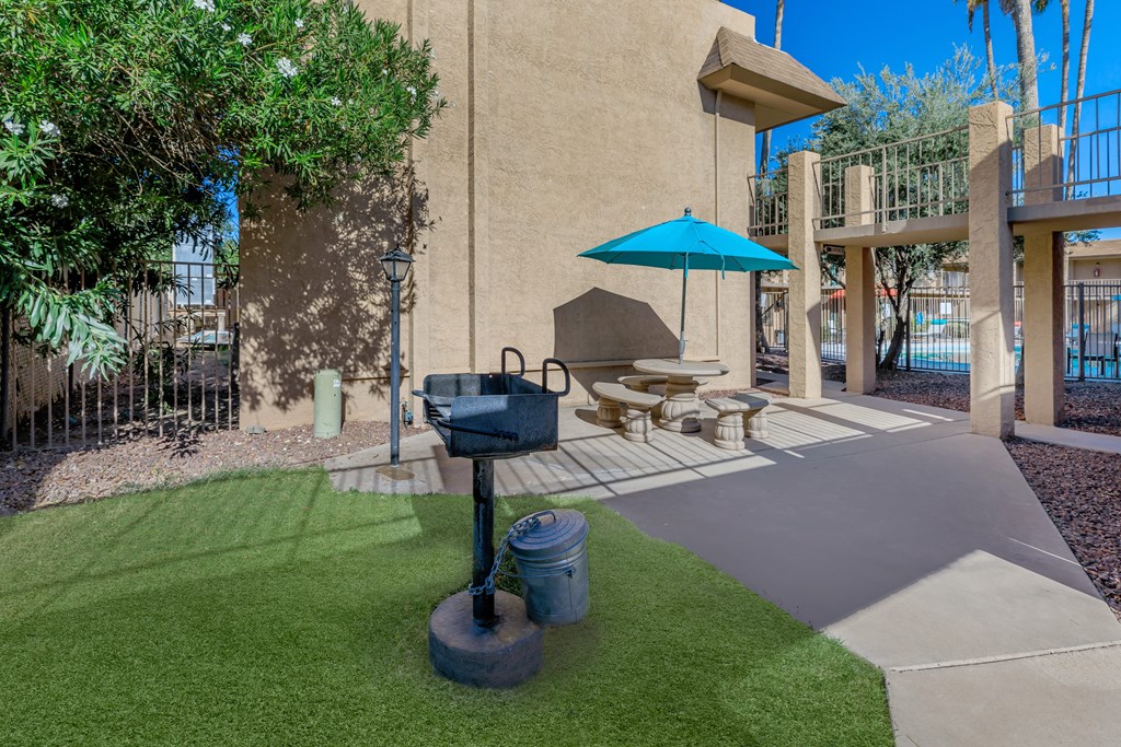 A patio with a blue umbrella and a grill.