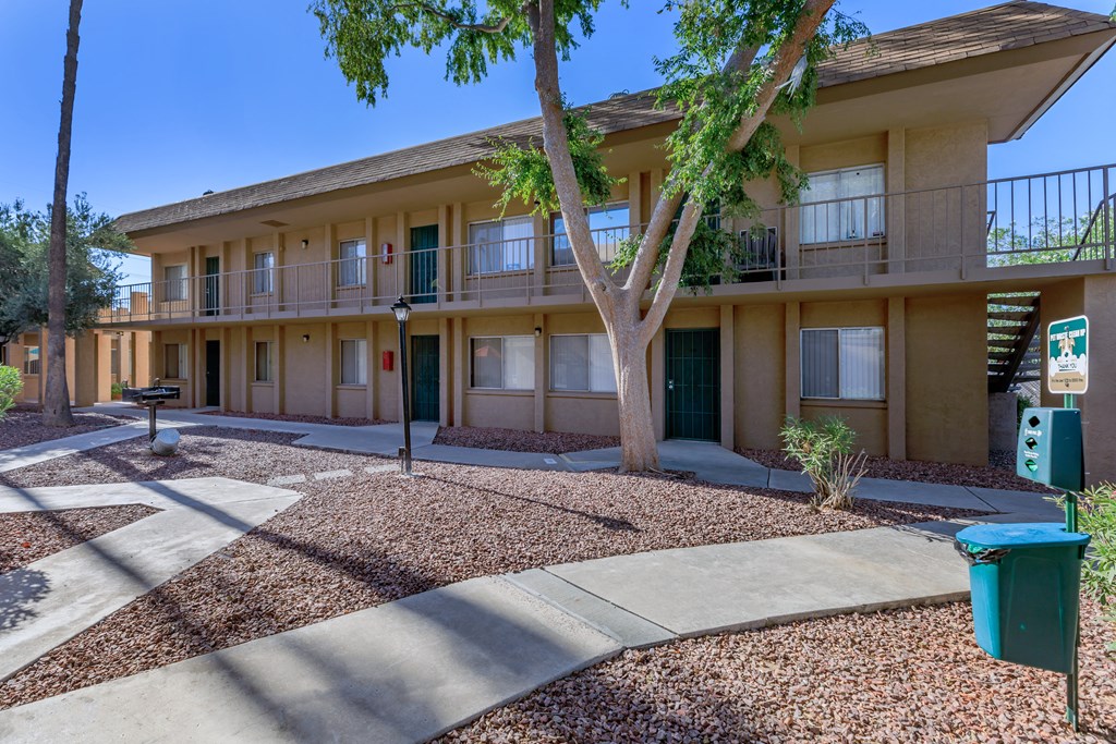 A tree in front of a building with a blue trash can to the right.