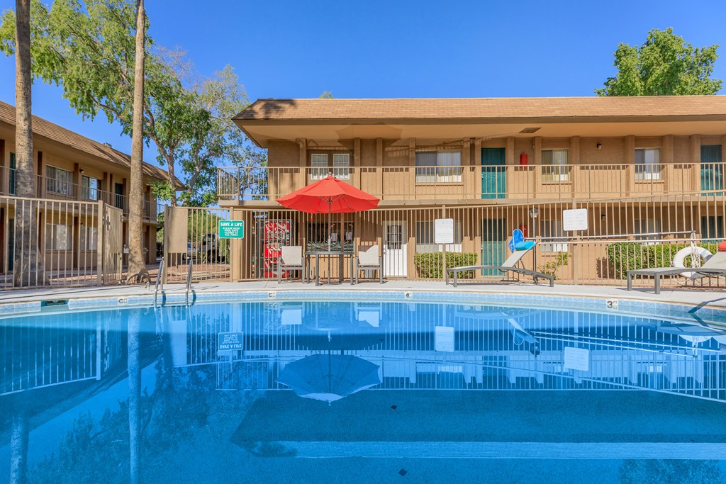 A swimming pool in front of a building with a red umbrella.