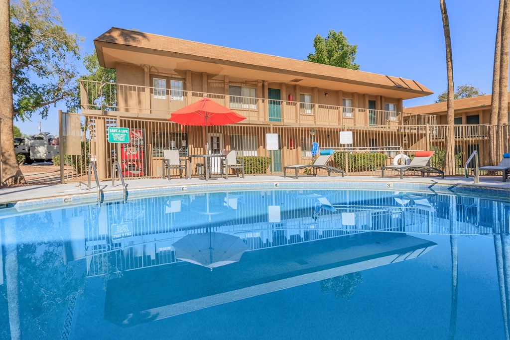 A swimming pool in front of a building with a red umbrella.