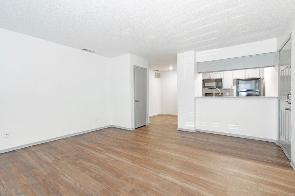 an empty living room with a hard wood floor and a kitchen