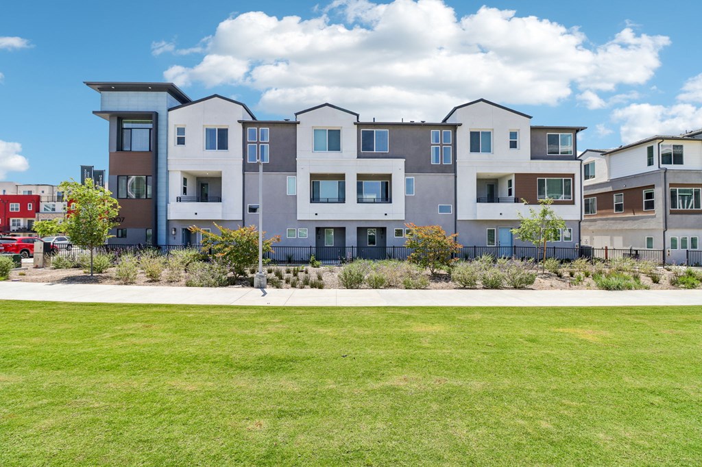 A row of modern townhouses with a green lawn in front.