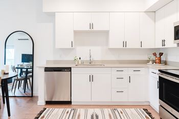 A modern kitchen with white cabinets and a striped rug on the floor.