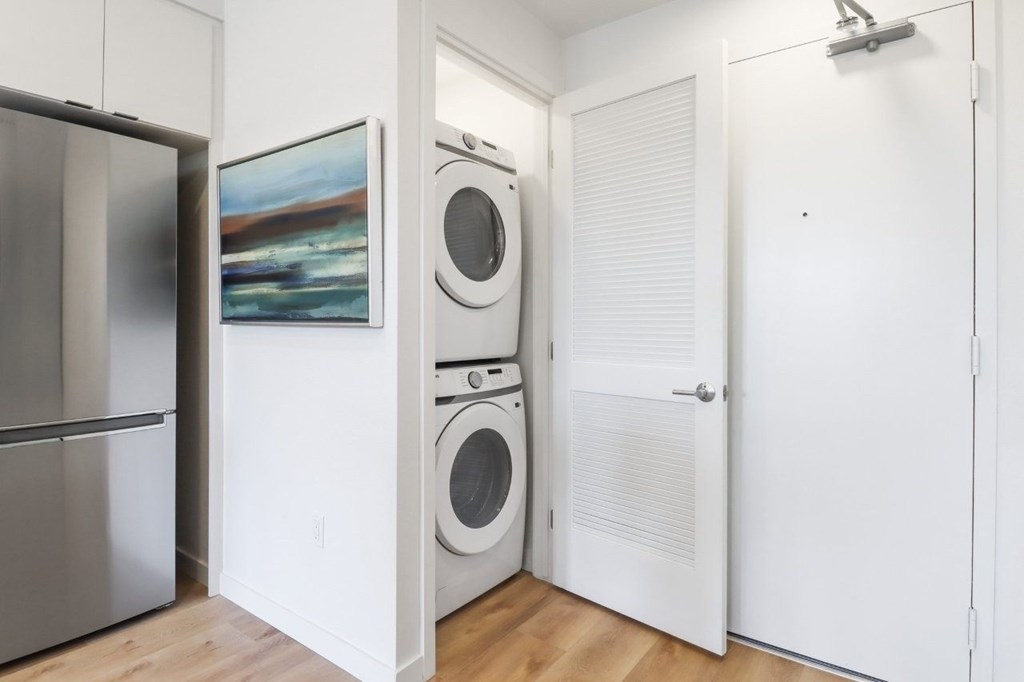 A white laundry room with a refrigerator, a washer and a dryer.